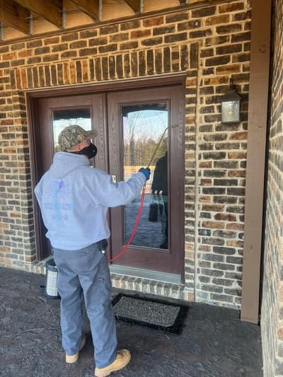 Technician treating around the front door and entry points of a brick home