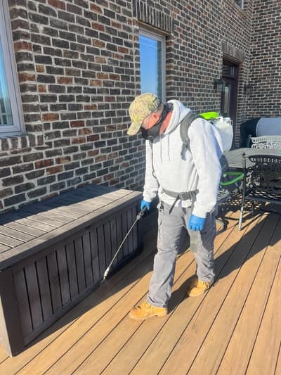 Technician with a backpack sprayer treating the perimeter around a deck